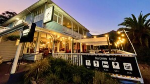 Un hotel con balcón, mobiliario exterior y un cartel que indica servicios como restaurante, bar y piscina.