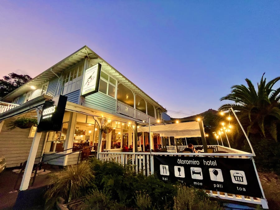 A hotel with a balcony, outdoor seating, and a sign indicating amenities like a restaurant, bar, and pool.