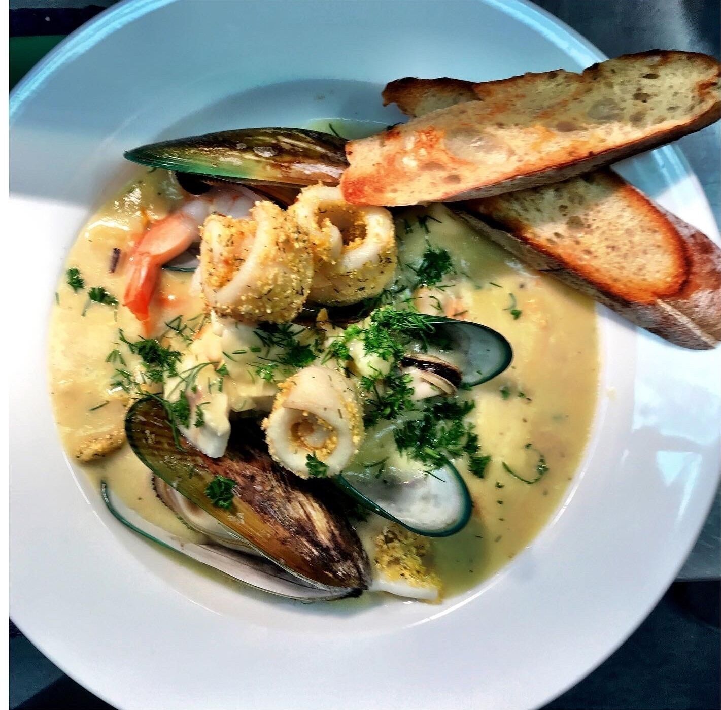 A seafood dish with mussels, clams, and bread on a white plate.