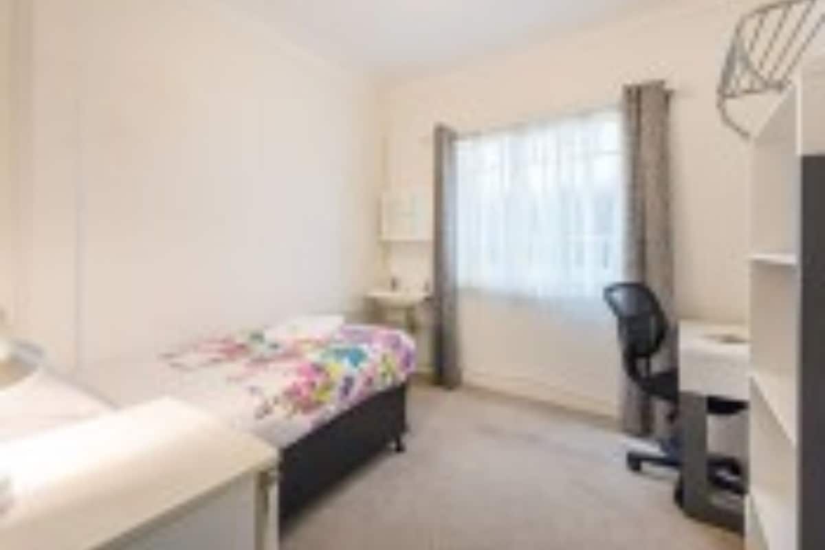 A small, neatly arranged bedroom with a bed, a desk, and a chair.