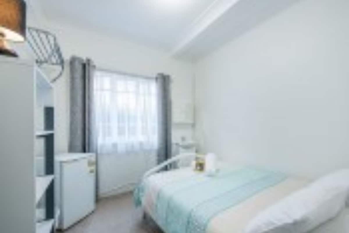 A small, clean room with a bed, a desk, and a window with curtains.