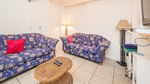 Una sala de estar con dos sofás estampados, una pequeña mesa redonda de mimbre, una lámpara y un mueble para televisor.