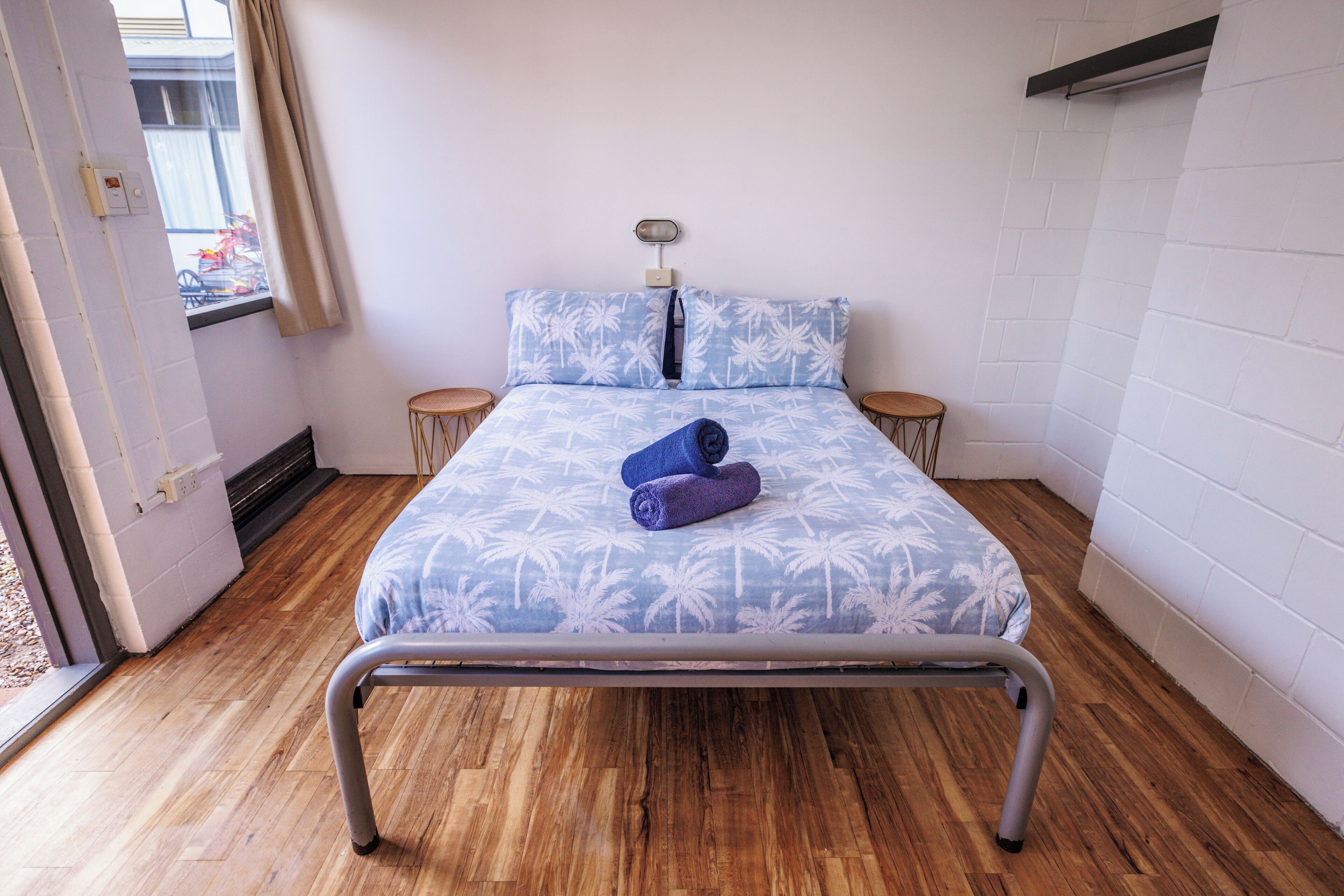 A single bed with a metal frame, a blue and white patterned bedspread, two pillows, and two bedside tables.