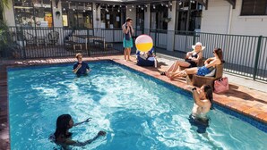 A swimming pool with people around it, a fence, and a building in the background. - YHA Coolangatta Gold Coast (Bilinga)