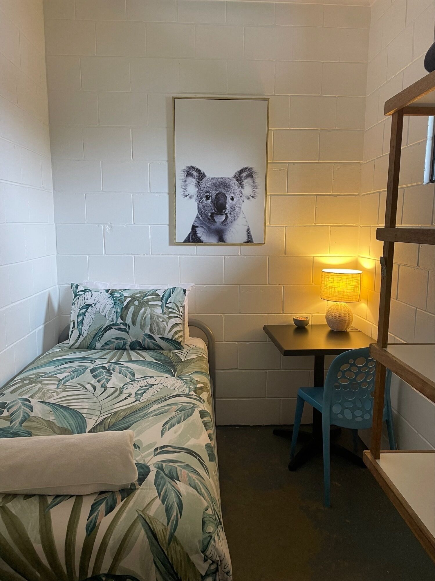 A small, compact room with a bed, a table with a lamp, and a chair.
