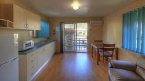 Cuina compacta amb frigorífic, microones, rentapelats i armaris de fusta. Hi ha una zona de dinar amb taula i cadires, i una porta corredissa de vidre que dona a un patio exterior.