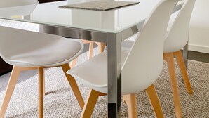 Un espace repas moderne avec une table à plateau en verre, des chaises blanches et un plancher en bois.