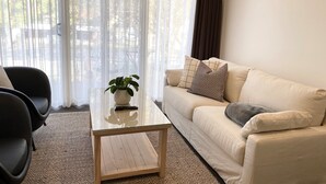 Un salon avec un canapé beige, une table basse en verre sur laquelle est posée une plante en pot, et un fauteuil noir.