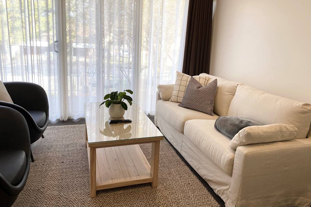 A living room with a beige sofa, a glass coffee table with a potted plant, and a black chair.