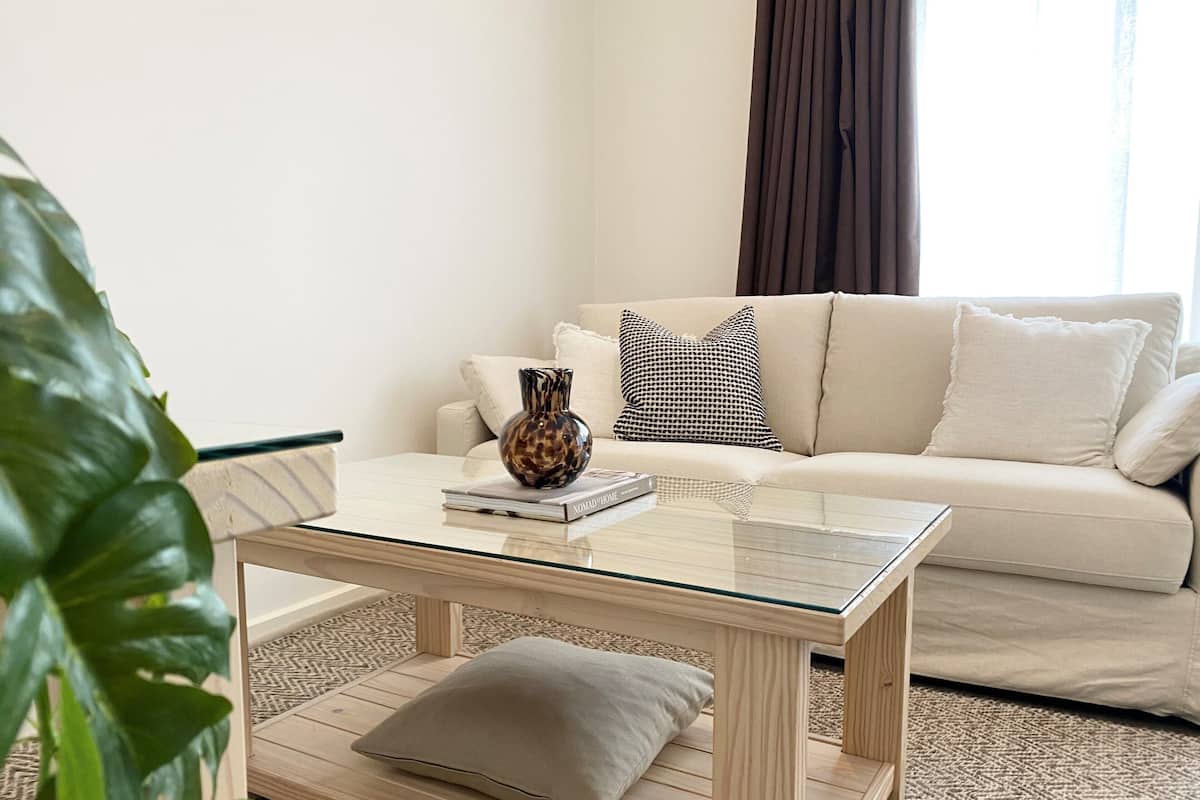 A living room with a glass-top coffee table, a sofa, and a patterned pillow.