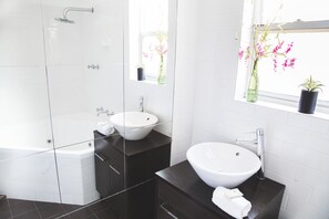 A modern bathroom with a bathtub, two sinks, a vanity, and a window with flowers. - Angaston Mews Apartments (Angaston)