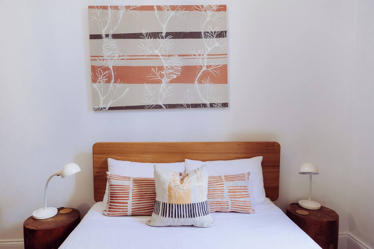 A neatly made bed with striped pillows and a wooden headboard, flanked by bedside tables with lamps.