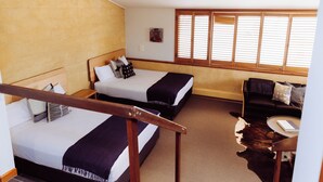 Habitación de hotel con dos camas, una escalera de madera, un sofá de cuero y un ventanal con persianas.