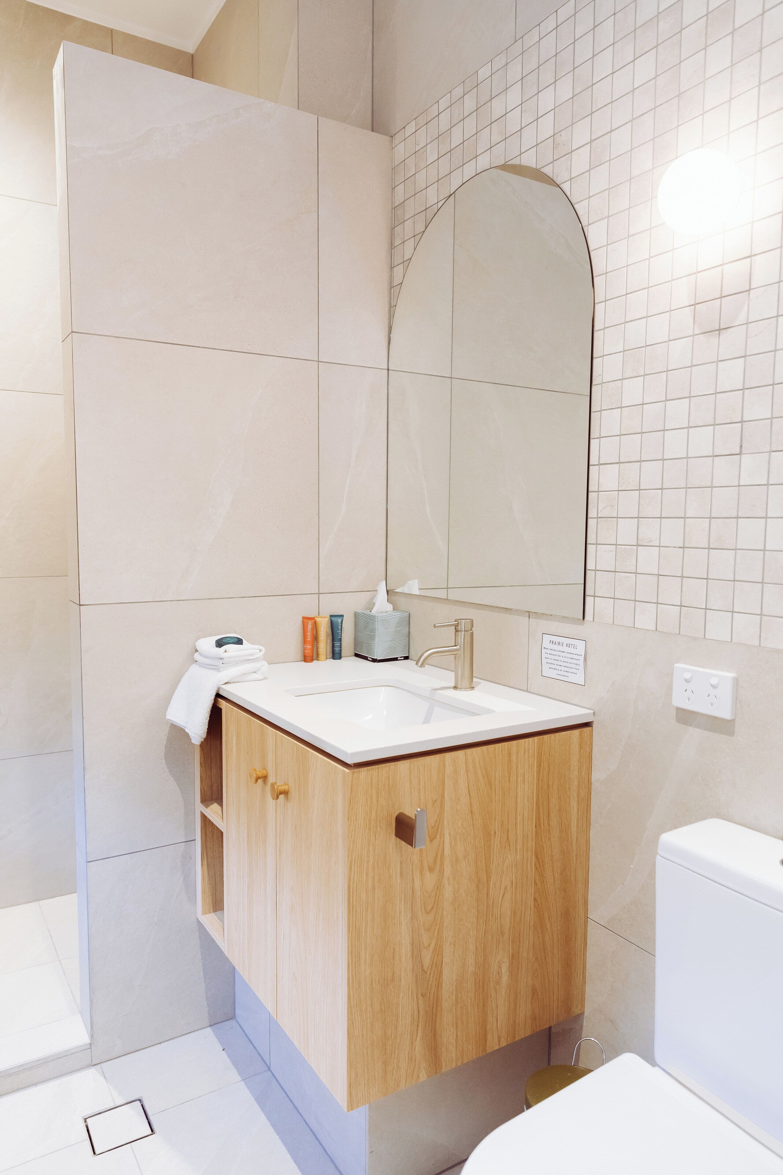 A modern bathroom with a white sink, wooden cabinet, and a large mirror.