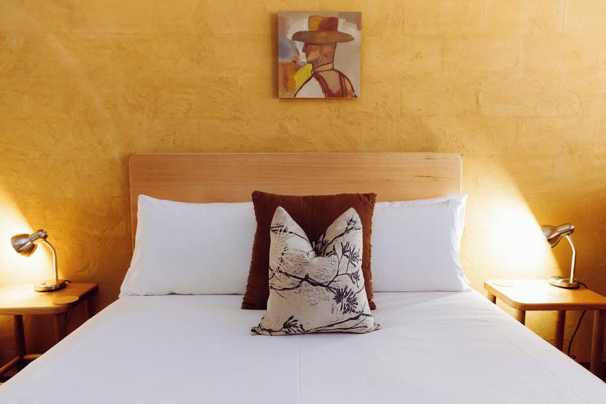 A neatly made bed with white linens and two pillows, one with a floral pattern.