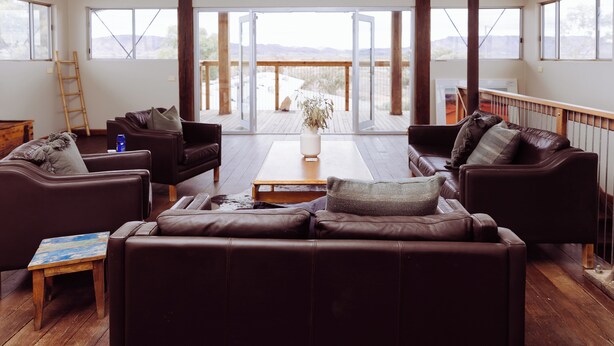 Un salón comedor amplio con sofás de cuero, una mesa de centro de madera y ventanas grandes con vistas al exterior.