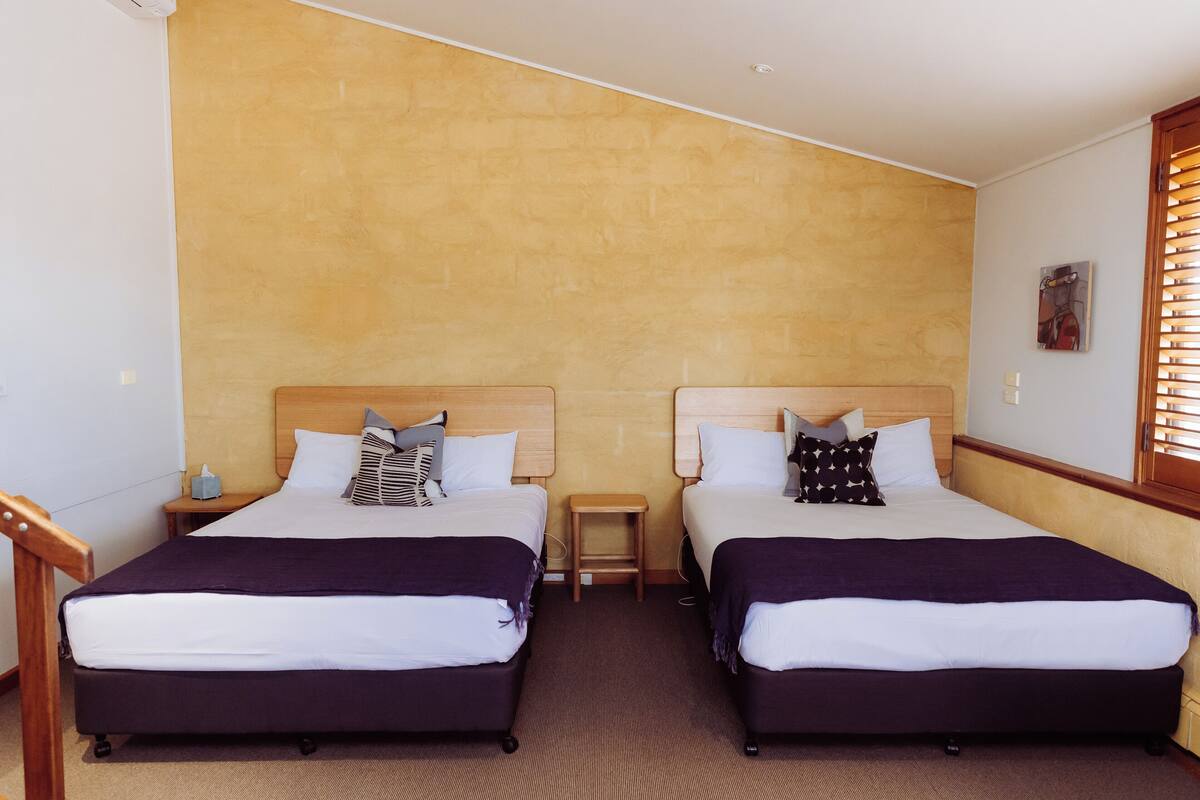 A hotel room with two beds, a small wooden nightstand, and a wall-mounted artwork.