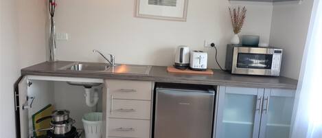 Een kleine keuken met een spoelbak, een magnetron, een broodrooster en een koelkast.