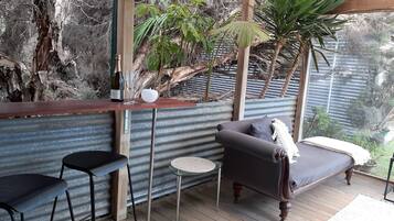 Una terraza de madera con una zona de estar acolchada, una mesa pequeña y una botella de vino.