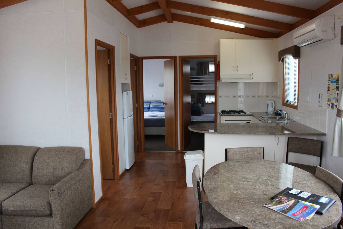 A compact kitchen with a dining area, wooden beams, and a refrigerator.