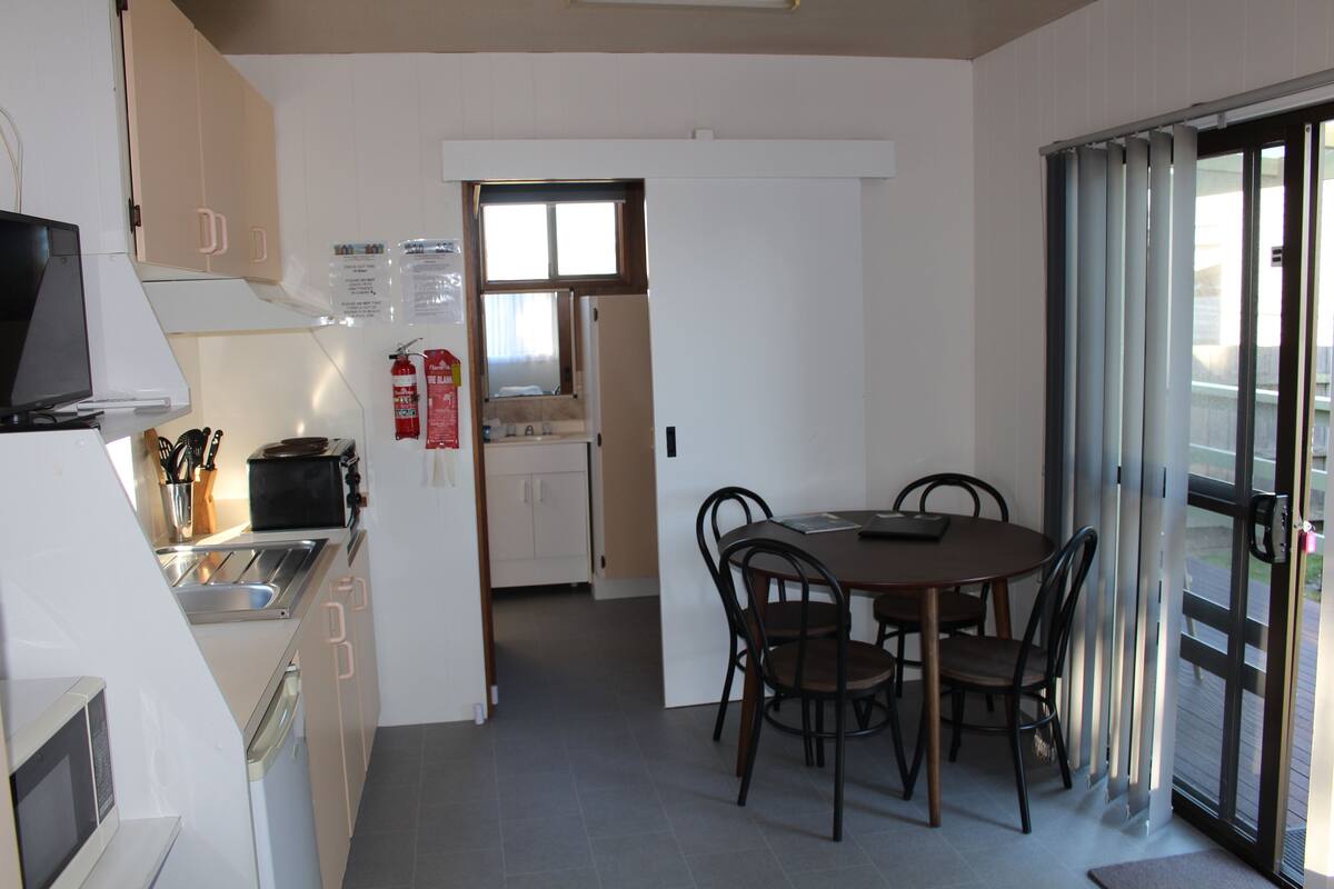A compact kitchen with a microwave, stove, and sink, leading to a dining area with a table and chairs.