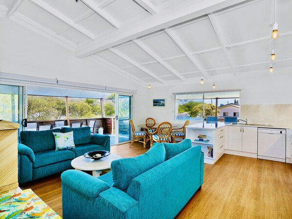 A spacious living area with a large sofa, a dining table with chairs, and a kitchen area. - Blue River Apartments - Wooli Ocean - Waterfront (Wooli)