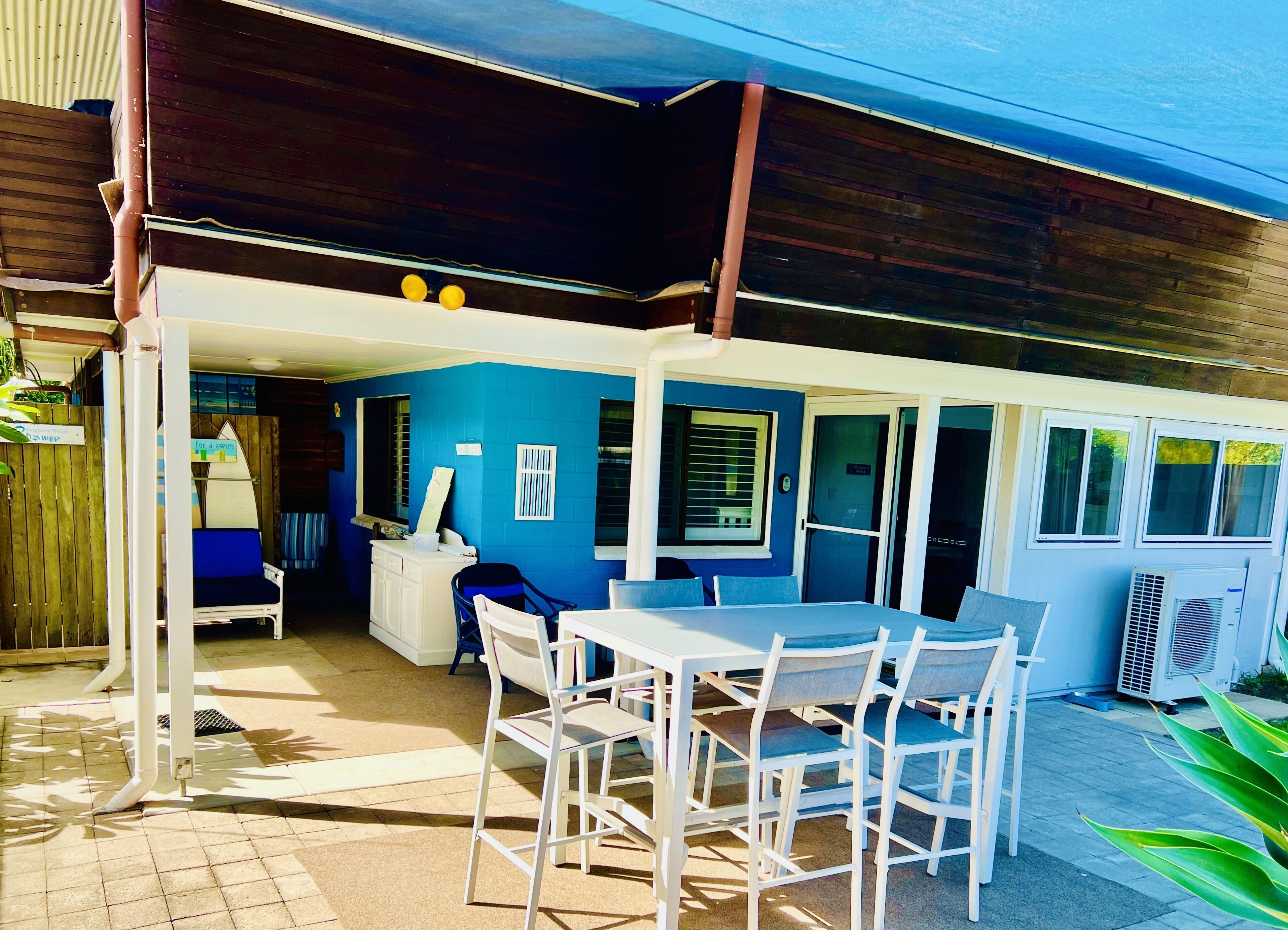 Un patio al aire libre con una mesa y sillas, un área de estar cubierta y una pared azul.