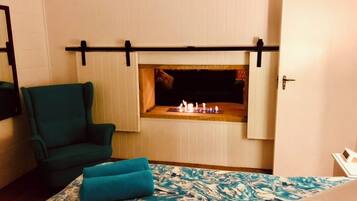 A room with a bed, a green armchair, a fireplace, and a door.