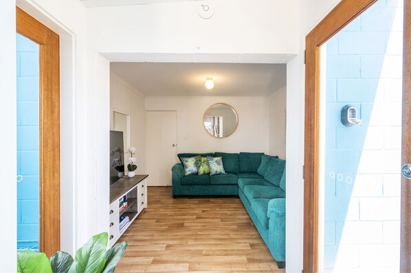 A cozy living room with a teal sofa, wooden flooring, a round mirror on the wall, and a small plant on the left.
