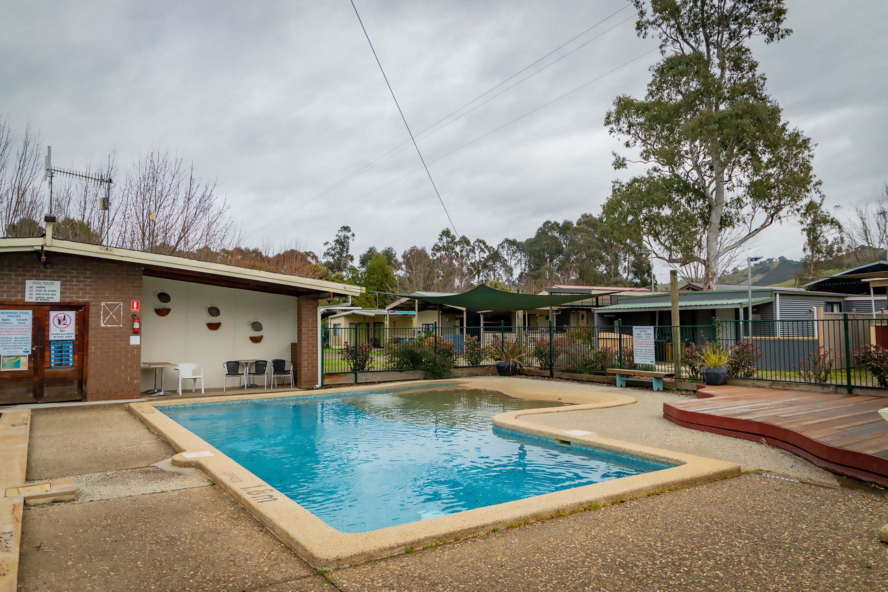 A swimming pool area with a brick building, outdoor seating, and a covered area.