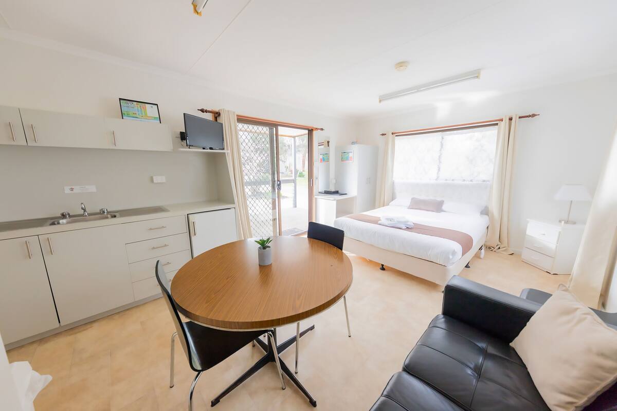 Quarto de hotel moderno com cozinha compacta, área de refeições, cama e sofá.