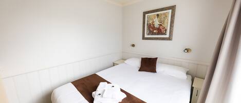 Cama bem arrumada com lençóis brancos e castanhos, um único travesseiro marrom e uma obra de arte emoldurada na parede.