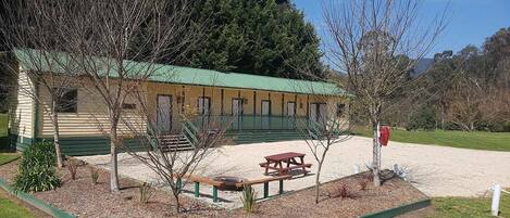 A rustic lodge with a green roof, a picnic table, and a gravel driveway.