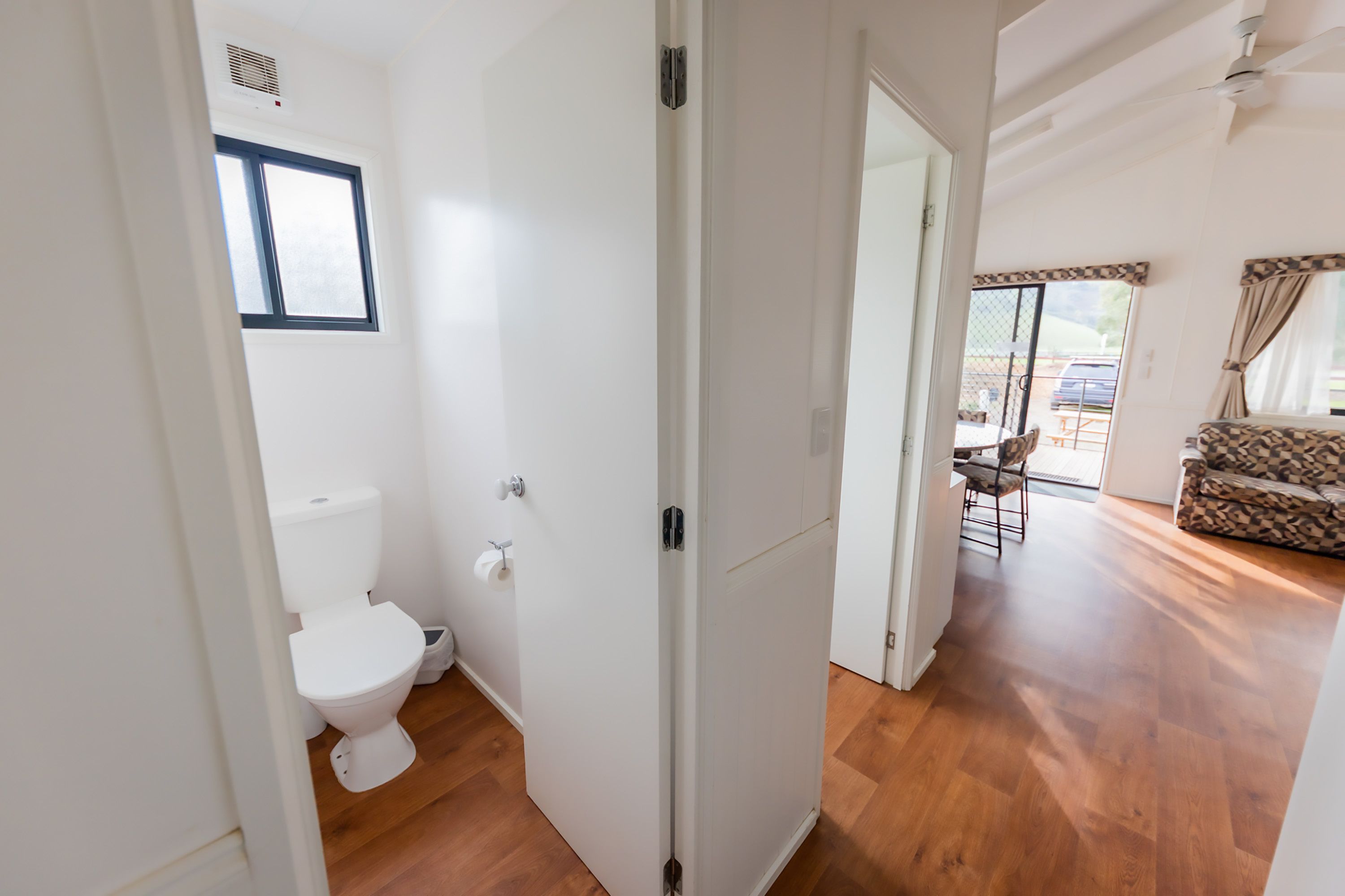 A room with a white toilet, wooden flooring, and a patterned sofa.