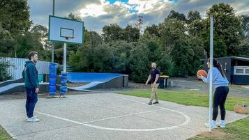 Quadra de basquete ao ar livre com cesta, área acolchoada azul e um jogador de basquete ao fundo.