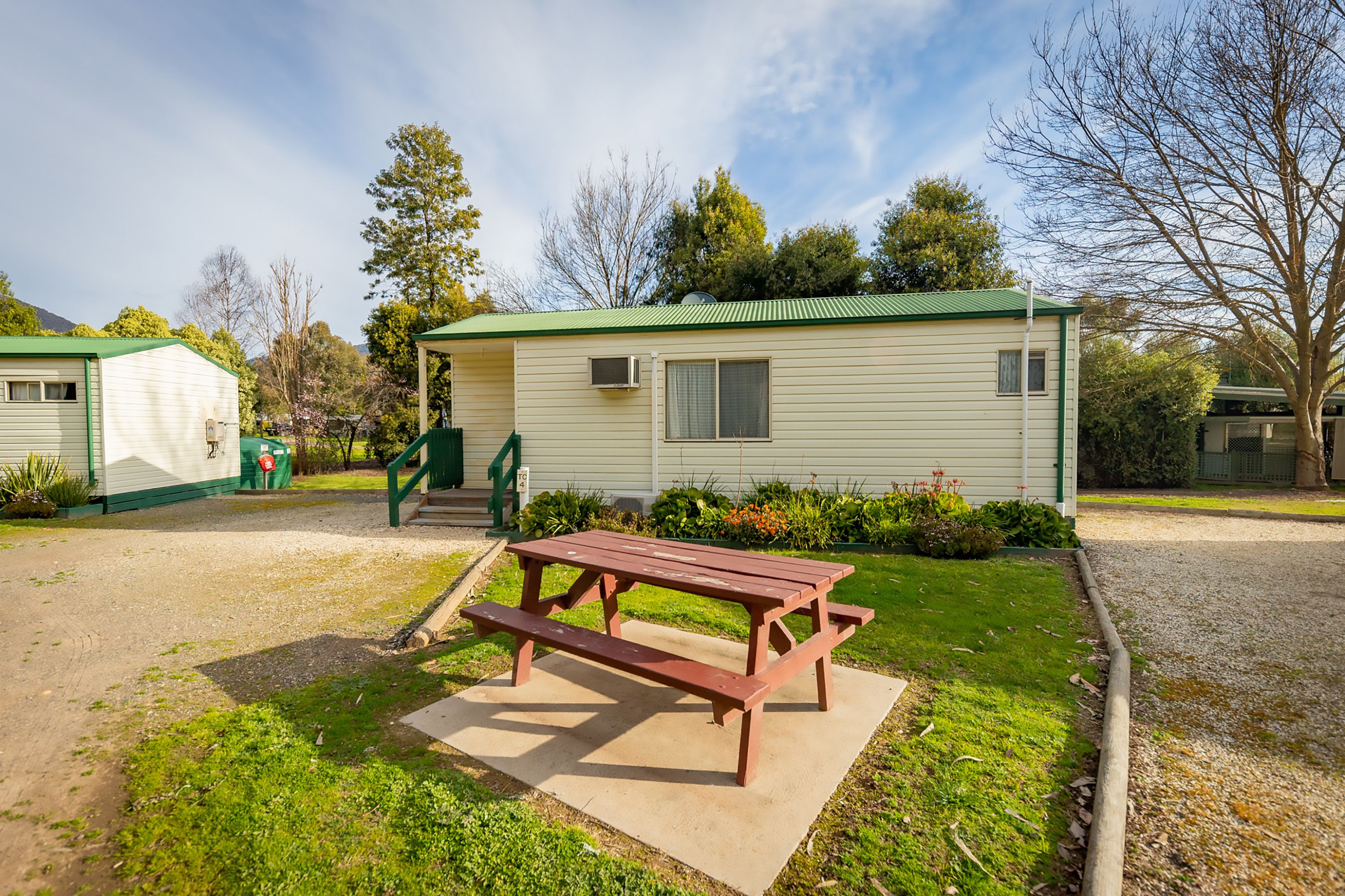 A mobile home with a picnic table in front, surrounded by a well-maintained lawn and a gravel path.