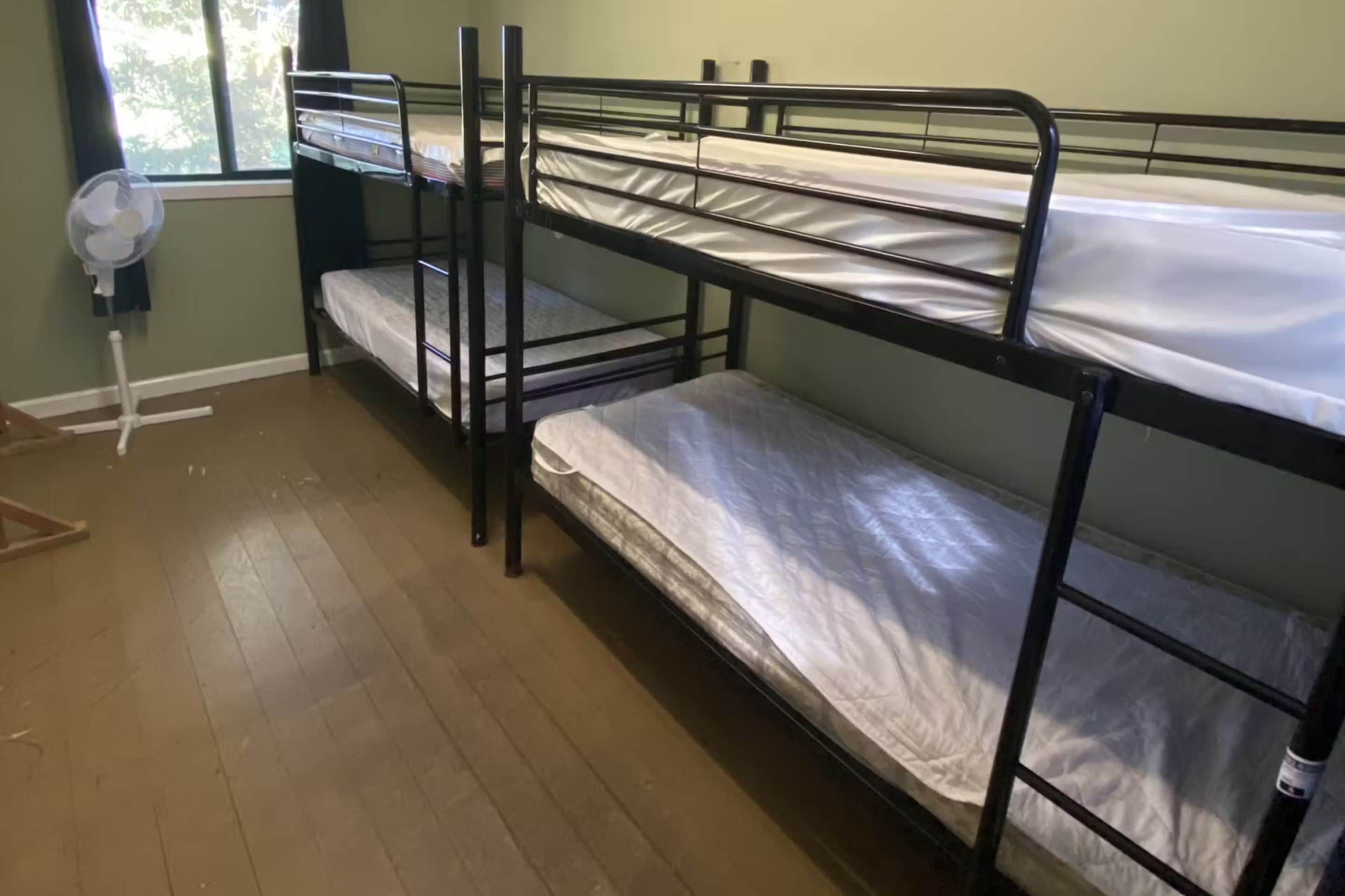 Una habitación con literas, un ventilador de pie y una ventana con cortinas.