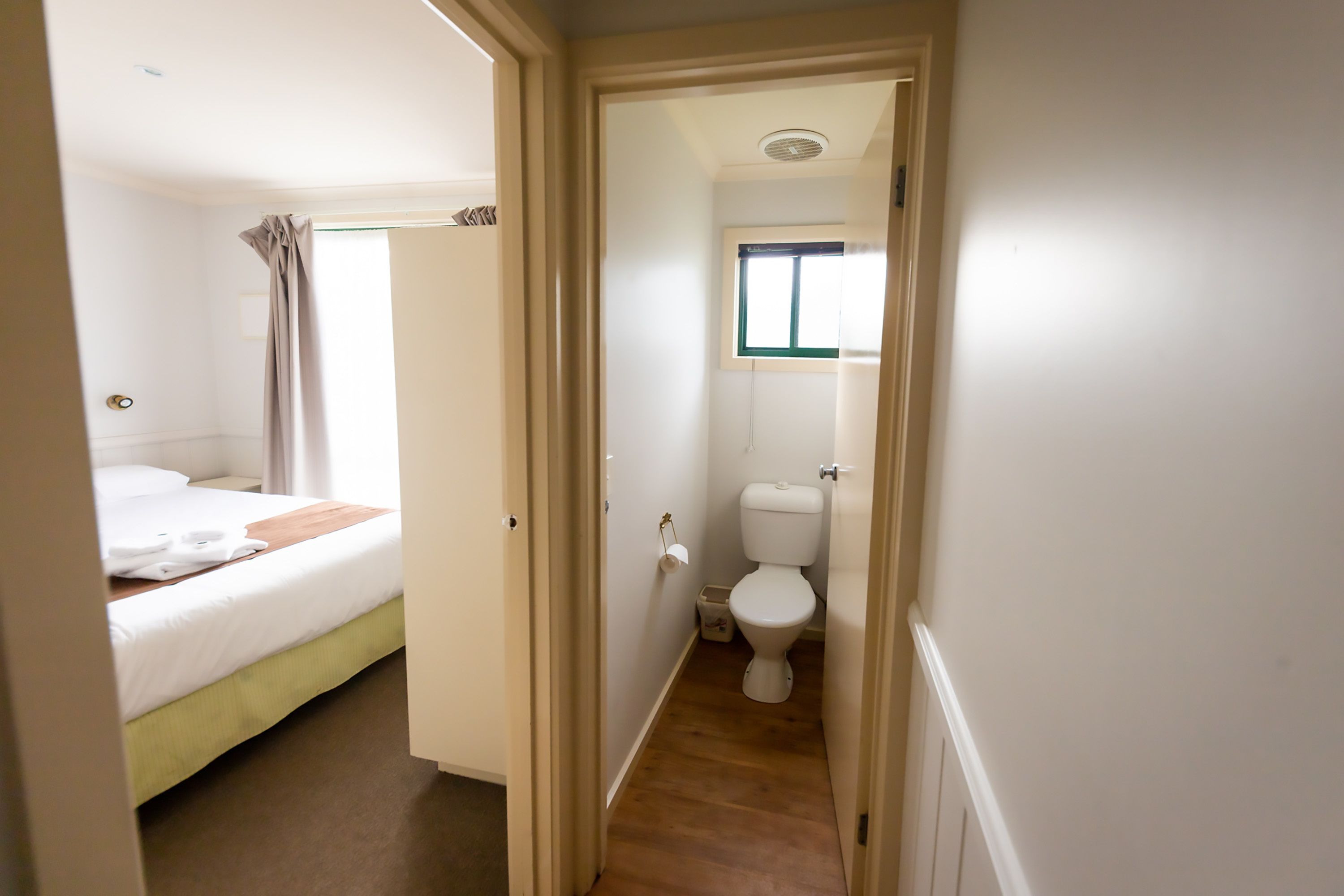 Un pasillo estrecho que conduce a un dormitorio con cama y un baño con inodoro y ventana.