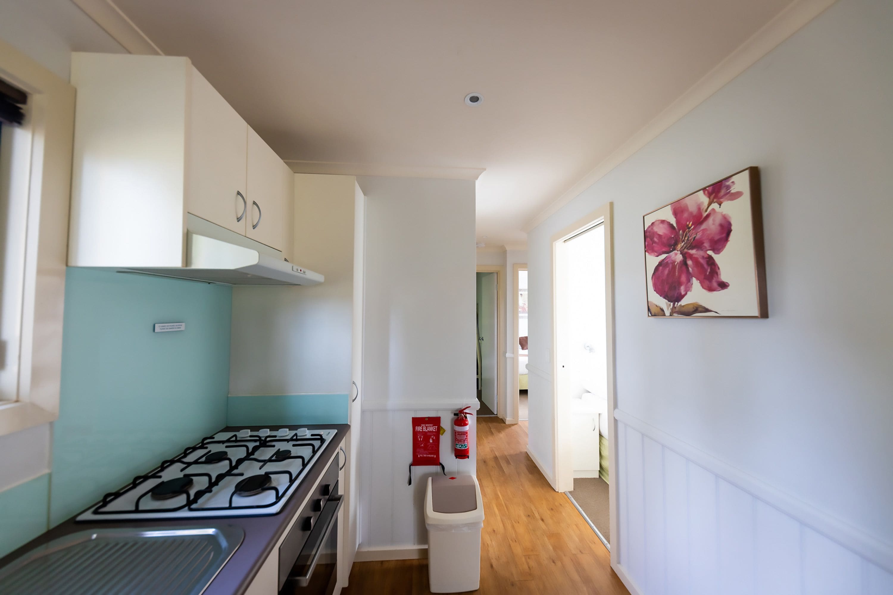 A narrow hallway with a kitchen area on the left, featuring a gas stove and cabinets. A fire extinguisher is mounted on the wall near the stove.