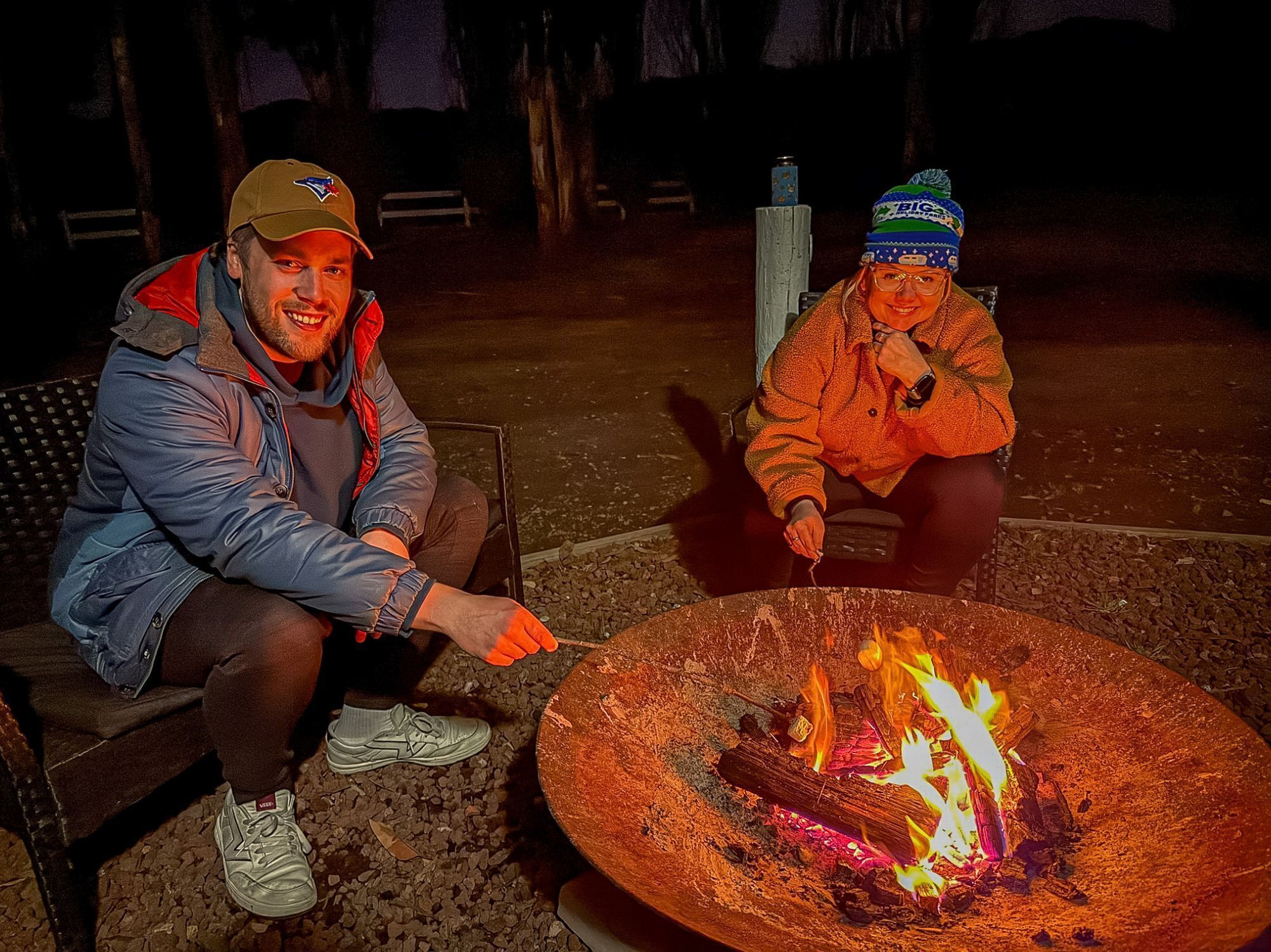 Two people sitting by a campfire at night.