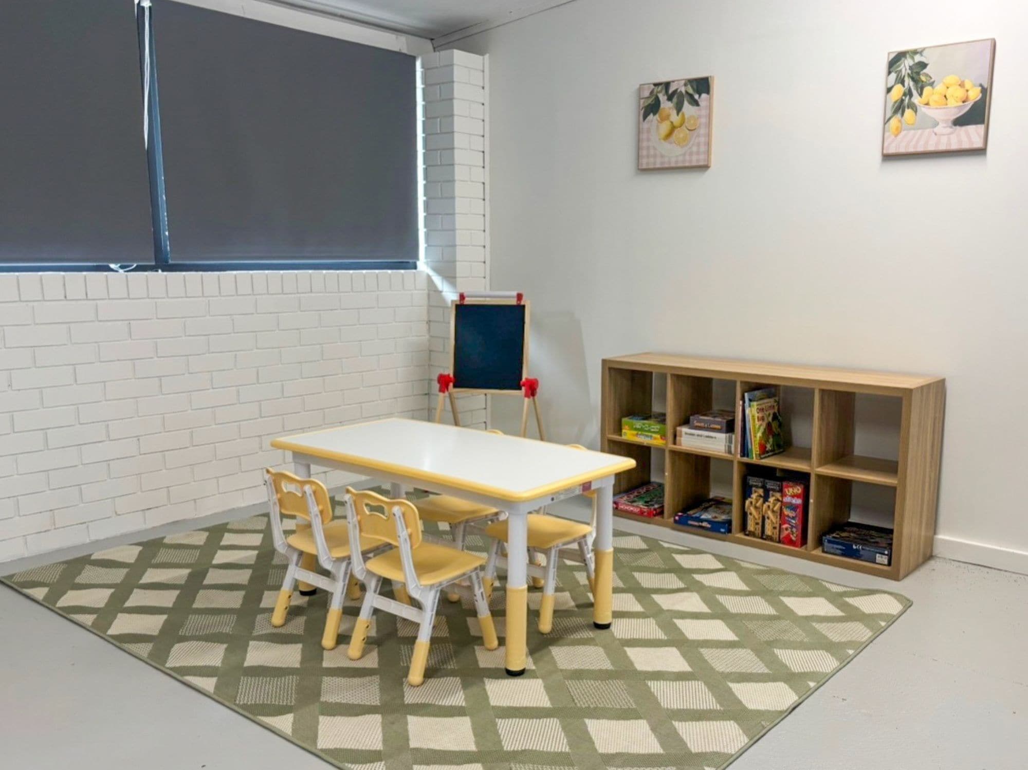 Une pièce avec une table et des chaises blanches, un tableau noir et une bibliothèque remplie de jeux.