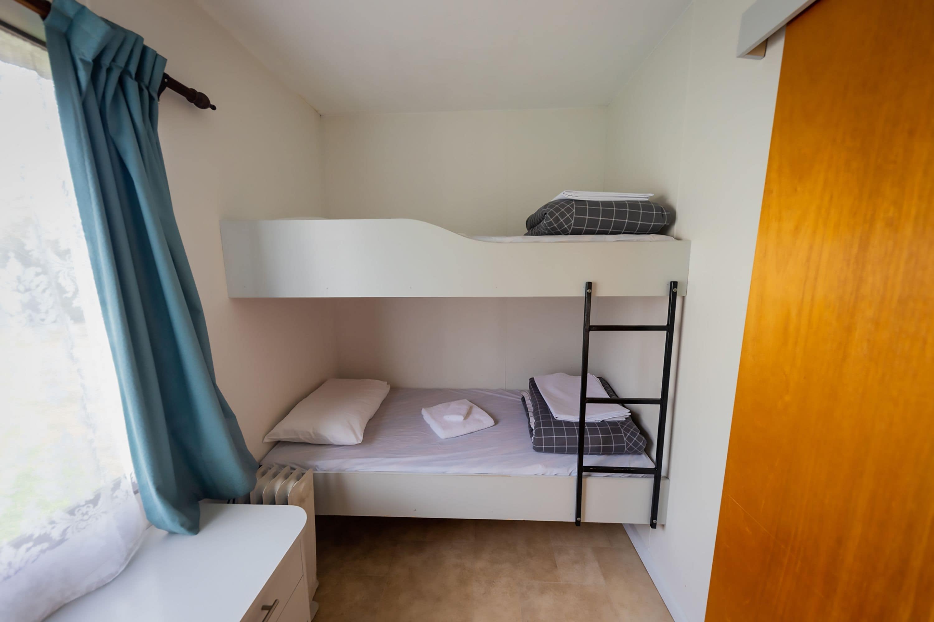 Habitación con literas, ventana, cortina y puerta de madera.