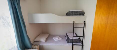 Habitación con literas, ventana, cortina y puerta de madera.