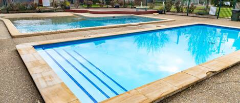 A rectangular swimming pool with blue tiles and a wooden edge, surrounded by a gravel area and a fence.