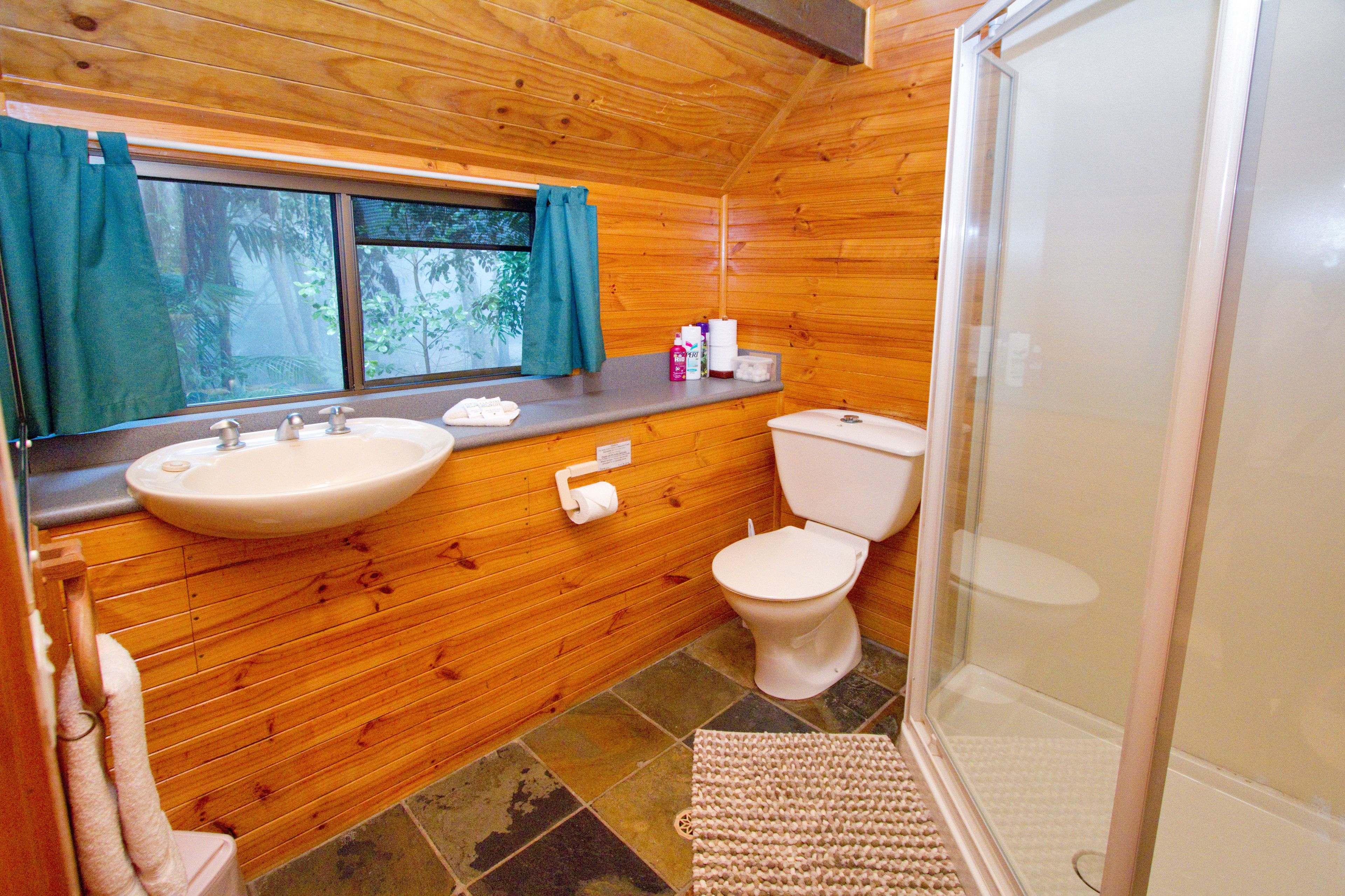 A wooden cabin bathroom with a sink, toilet, and shower.