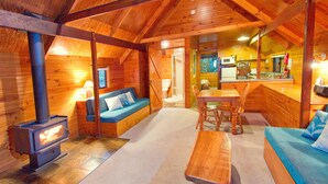 Ein gemütliches Blockhaus-Interieur mit Kaminofen, einer Couch, einem Esstisch und einer Küchenzeile.