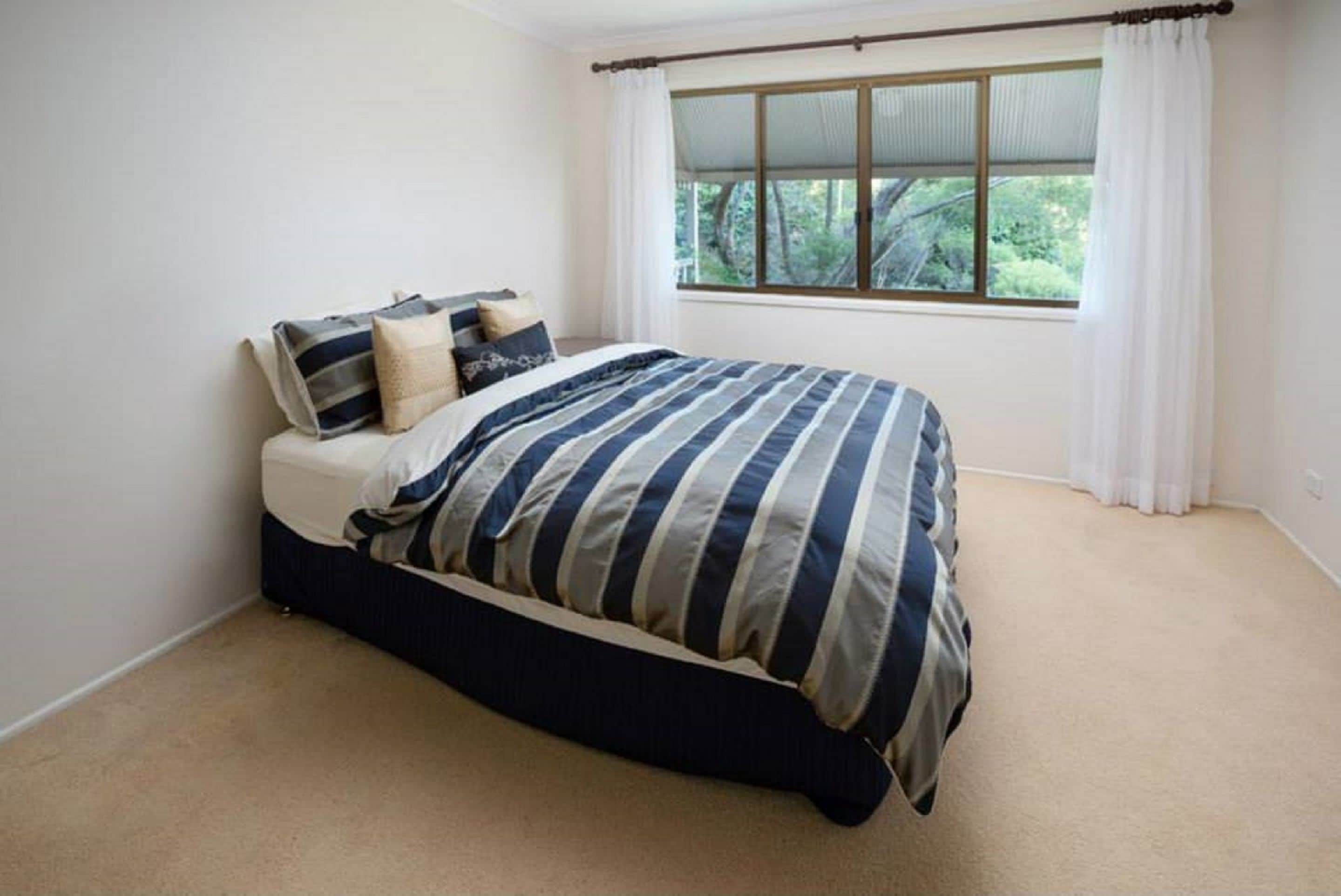 Une chambre à coucher avec un lit, une fenêtre avec des rideaux et une vue sur la verdure à l’extérieur.
