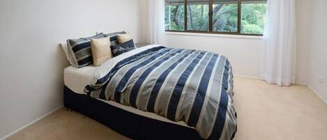 Une chambre à coucher avec un lit, une fenêtre avec des rideaux et une vue sur la verdure à l’extérieur.