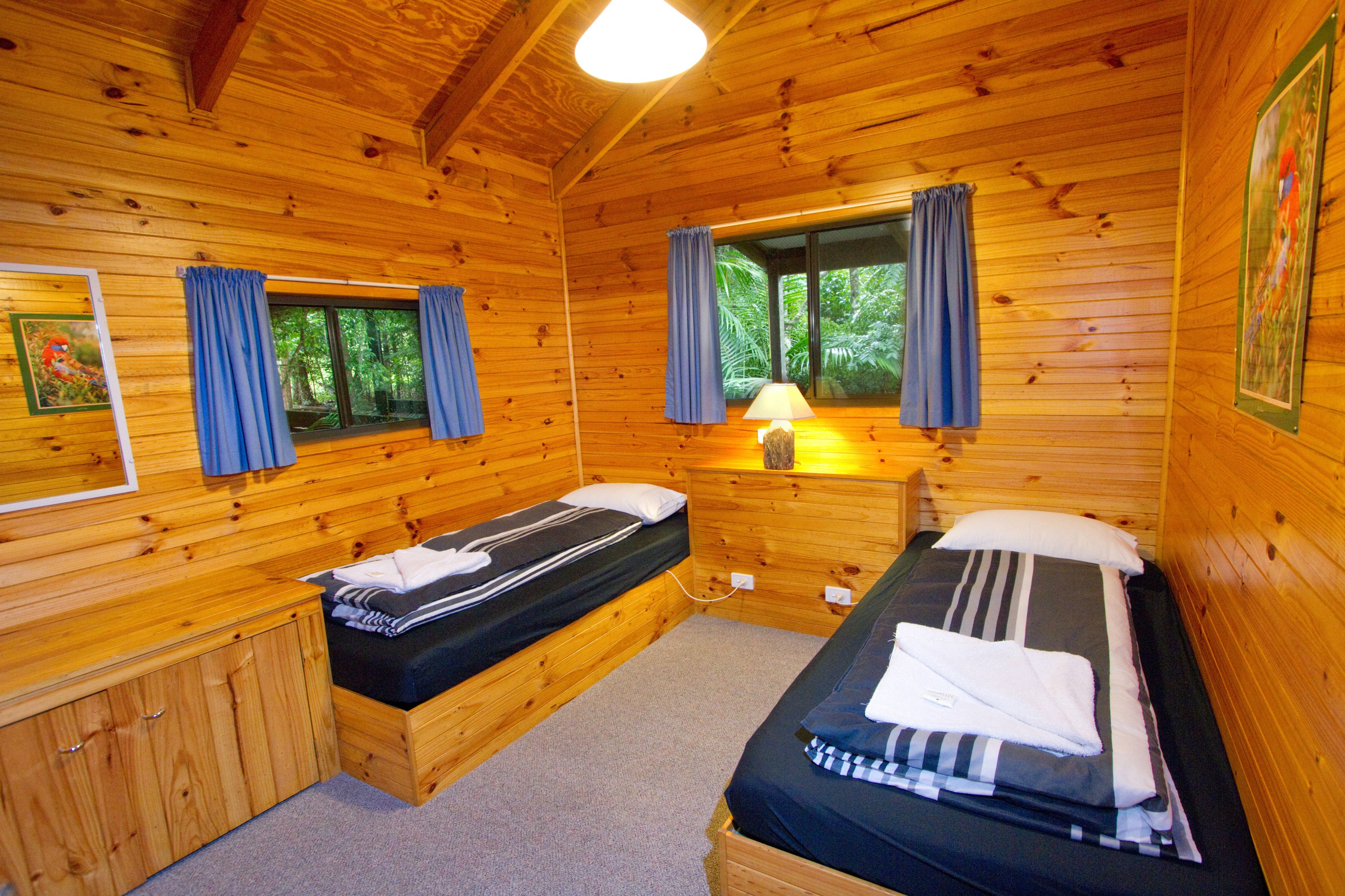 A cabin with two wooden beds, a window with curtains, a lamp, and a framed picture on the wall.