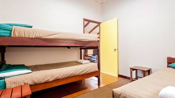 A dormitory room with two bunk beds, a wooden chair, a small table, and a door.